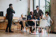 © qunica.com - Businesspeople collaborating on a project in a contemporary co-working space with a rustic interior design, featuring large windows and natural lighting, embodying a vibrant and productive workplace.