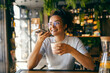 © Dusan Petkovic - Portrait of multiracial cheerful girl leaving voice message and drinking coffee in cafeteria.