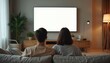 © Vadym - Young couple watches blank screen TV in modern minimalist living room. People relax on sofa at home. Family spending time together, enjoying content. Cozy home, leisure, technology, weekend activity.