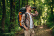© standret - Side view, standing, holding binoculars. Male tourist is with backpack in the forest