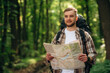 © standret - Searching the way, holding map. Male tourist is with backpack in the forest