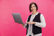 © anatoliycherkas - Smiling mature businesswoman holding laptop on pink background