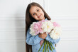© New Africa - Cute little girl with bouquet of beautiful peonies near white wall indoors
