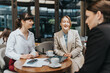 © qunica.com - Three business professionals discussing and networking in a relaxed coffee shop setting.
