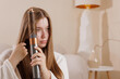 © st.kolesnikov - Woman using a modern hair curler at home, styling long hair, beauty routine, innovative device, healthy hair, selfcare.