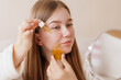 © st.kolesnikov - Woman applies yellow serum oil to face, skincare routine, moisturizing, beauty, healthy skin, hydration, wellness, daily cosmetic selfcare, glow, facial care.
