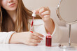 © st.kolesnikov - Applying red serum with a dropper, female hand, skincare routine, hydration, wellness, beauty care, glowing, healthy skin, modern lifestyle, cosmetic product.