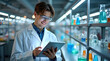 © Petro - Smiling young male scientist in a lab coat using a tablet amidst colorful glassware.