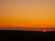 © mark_gusev - Renewable wind turbines in a vast field at warm orange sunrise. Alternative sustainable source of electric energy. he scene is peaceful and serene, with the turbines standing tall. Copy space