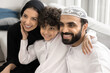 © fizkes - Unity in tradition and warmth in love. Family portrait happy Arabic couple with little son in faith based Islamic clothing cuddle on couch. Affectionate small boy tender touch faces of beloved dad mom