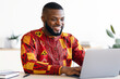 © Prostock-studio - Successful Black Businessman In African Traditional Clothes Sitting At Workplace In Office, Happy Male Entrepreneur In Ethnic Shirt Working With Laptop Computer At Desk, Typing On Keyboard And Smiling