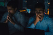 © S photographer - Two anxious professionals focus intently on their laptops in a dimly lit office during long working hours.