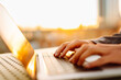© maxbelchenko - Close-up of young business woman's hands typing on a keyboard in the sunset. Female freelancer working on a laptop and enjoying the sunset. Business concept.