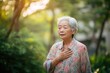 © Lyashko-Ai - An elderly Asian woman with hand on chest in a serene outdoor setting, looking concerned.