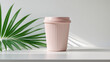 © A2ZDesign - Pink coffee cup with lid and palm leaf on white table natural light