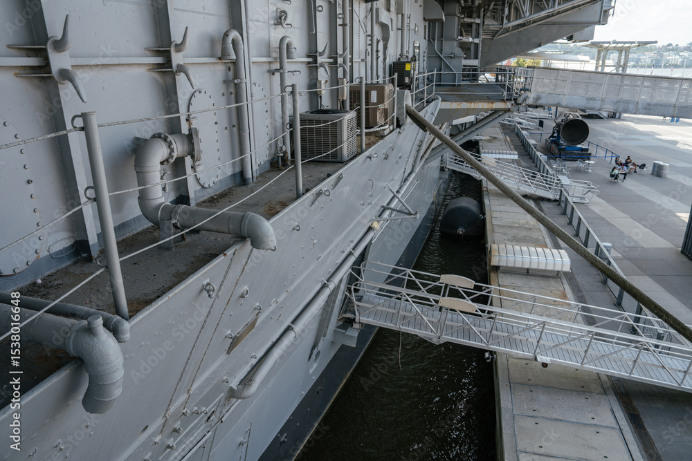 The image shows the detailed side of a docked aircraft carrier with ...