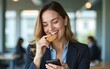 © si - Smiling businesswoman eating a cookie while using mobile phone in the office. High quality