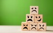 © wu - Wooden blocks with sad faces stacked in a pyramid shape on a blurred green background.  Sadness, depression, or negative emotions concept. ideal for mental health or emotional well-being concepts.