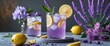 © Lasvu - Glass of cold lavender lemonade with lemons and flowers on grey table, featuring empty space for text.