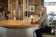 © WavebreakMediaMicro - Woman sitting at curved wooden bar counter in brewery holding amber beer glass, copy space