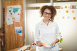 © WavebreakMediaMicro - Female designer standing at desk in creative office workspace holding color fan deck and red pencil