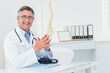 © WavebreakMediaMicro - Smiling male physician wearing lab coat at desk in clinic with stethoscope, spine model, copy space