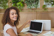 © WavebreakMediaMicro - Female professional turning laptop screen toward viewer at wooden desk in coffee shop with papers