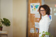 © WavebreakMediaMicro - African American woman wearing shirt standing by board with world map in office, copy space