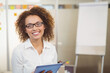 © WavebreakMediaMicro - Smiling businesswoman holding tablet and standing by flip chart with sticky notes in meeting room
