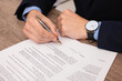 © New Africa - Man putting signature on document at wooden table, closeup