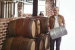 © Wavebreak Media - Man holding stainless steel keg inside brewery storage room with oak barrels and tanks, copy space