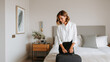 © dinatychynska - Stylish woman in elegant outfit packing suitcase in hotel room. Solo traveler preparing for summer trip. Cozy modern interior, business or vacation mood.