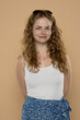 © vladimirfloyd - Young woman with curly hair and sunglasses on head, wearing white top and blue floral skirt. Warm background, natural smile, studio portrait