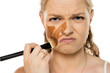 © vladimirfloyd - Young woman with intense frown and disgusted expression applying wrong shade of foundation, showing multiple streaks of too-dark makeup on face against white background
