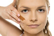 © vladimirfloyd - Young woman with calm expression showing different foundation swatches on cheek, demonstrating makeup shade testing with hand against face against white background