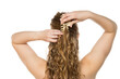 © vladimirfloyd - Rear view of young woman placing beige claw clip in her long wavy blonde hair, demonstrating half-up hairstyling process against white background