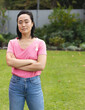 © Wavebreak Media - Asian woman standing with arms crossed in backyard garden showing pink awareness ribbon