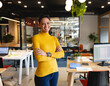 © Wavebreak Media - African American woman in mustard turtleneck standing and smiling at office with laptops and plants