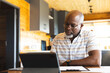 © Wavebreak Media - Senior African American man sitting at kitchen table writing on clipboard and checking tablet