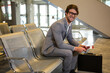 © Wavebreak Media - Male traveler in suit sitting at airport holding passport with briefcase by escalator, copy space
