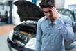 © Wavebreak Media - Man standing in auto repair workshop inspecting engine under open hood of black sedan, copy space