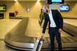 © Wavebreak Media - Mid adult businessman pulling suitcase from conveyor belt at baggage claim with screens, copy space