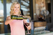 © Wavebreak Media - Adult woman pouring red wine from green bottle into glass at winery bar with empty glasses