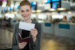© Wavebreak Media - Female traveler wearing blazer smiling and holding passport and boarding pass at airport check-in