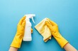 © Serhii - Hands Wearing Rubber Gloves Holding Spray Bottle and Cloth for Home Cleaning on Soft Blue Backdrop