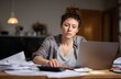 © ryker - Young businesswoman focused on her laptop, surrounded by paperwork and calculator, conveying sense of concentration and determination in home office setting