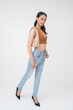 © Mdv Edwards - Confident young Filipino woman walking gracefully wearing a brown top and light blue jeans, isolated on a white background