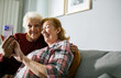 © Marko Geber - Senior lesbian couple laughing while video chatting with family on smartphone at home