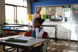 © Wavebreak Media - African American girl wearing denim jumper raising hand at desk in primary classroom with notebook