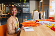 © Wavebreak Media - African American woman cutting orange fabric using sewing tools at wooden table in fashion studio